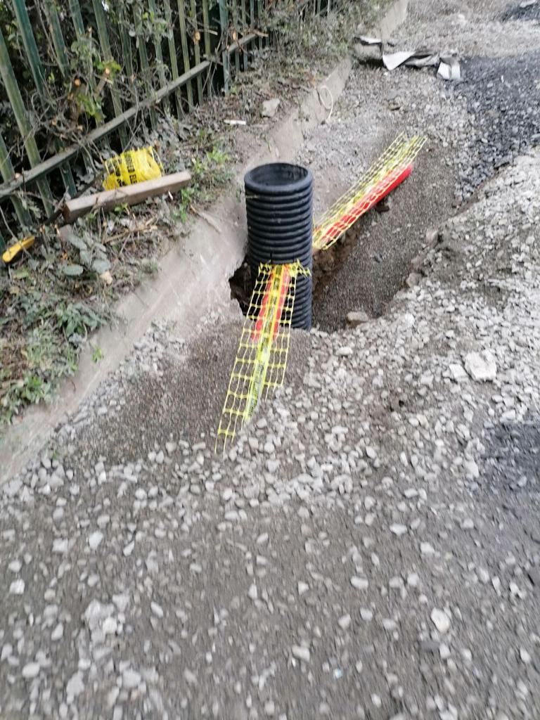 construction site with a black pipe and caution tape on a gravel path